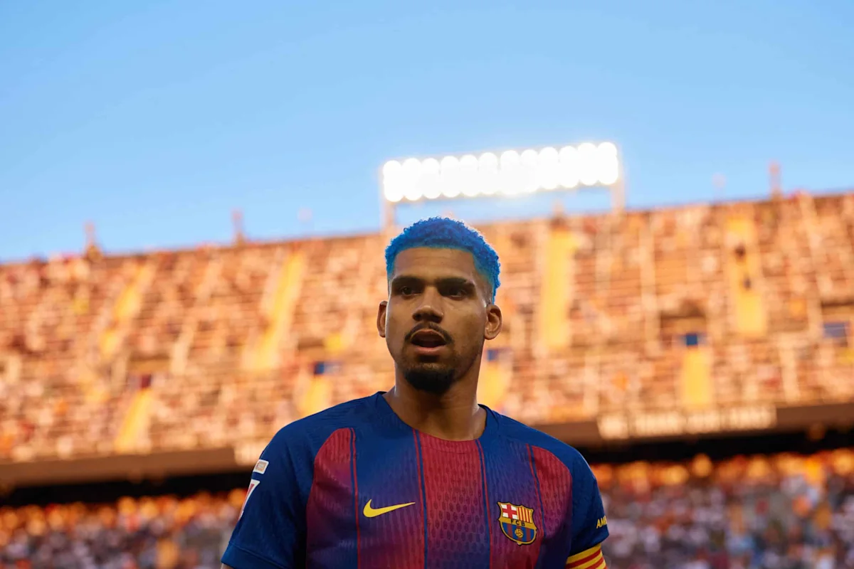 Ronald Araujo berseragam Barcelona berpose tegas dengan latar belakang stadion Camp Nou